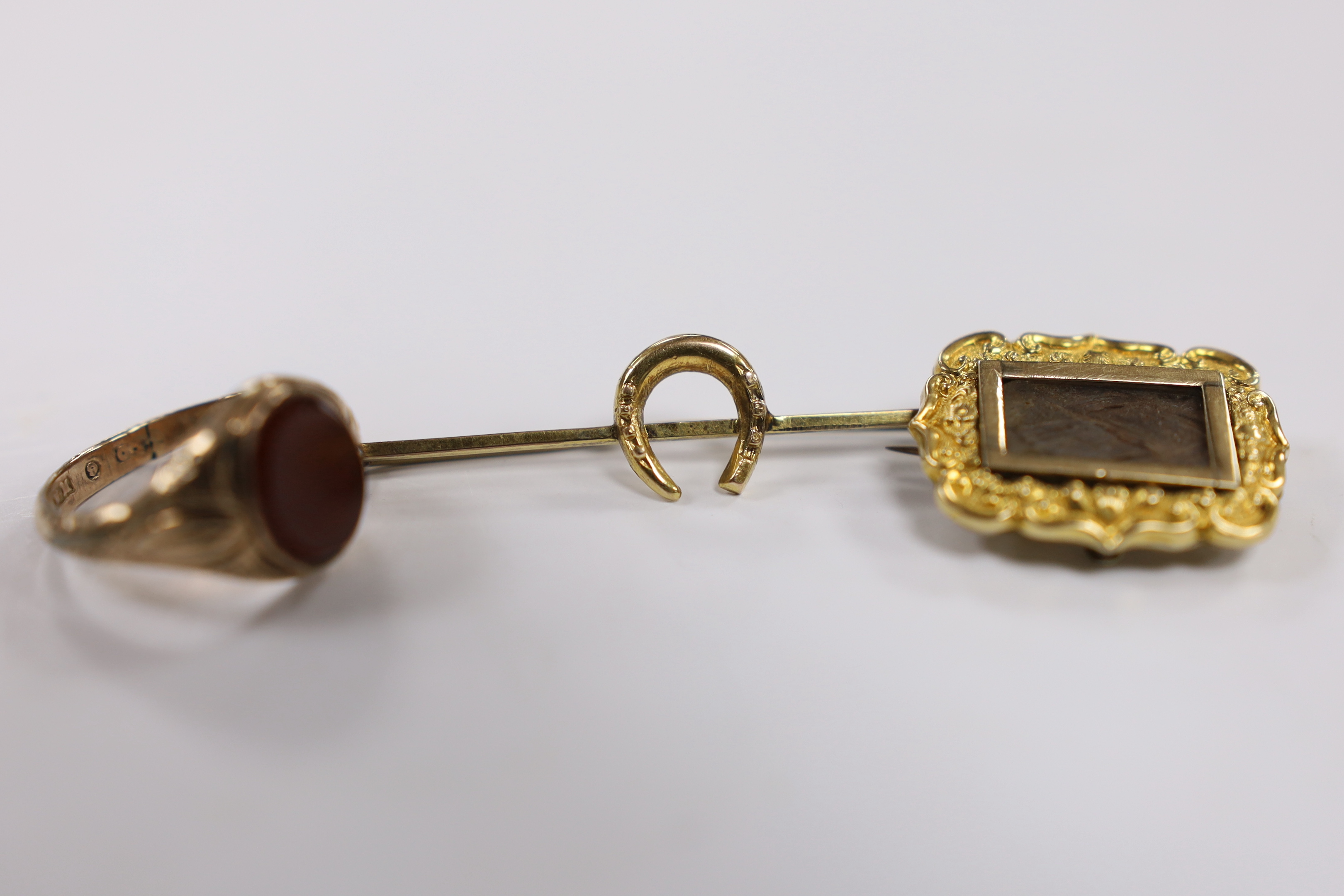A Victorian 9ct and carnelian set signet ring, size L, an early Victorian yellow metal and plaited hair set mourning brooch, dated 1842 and a 9ct horseshoe bar brooch.